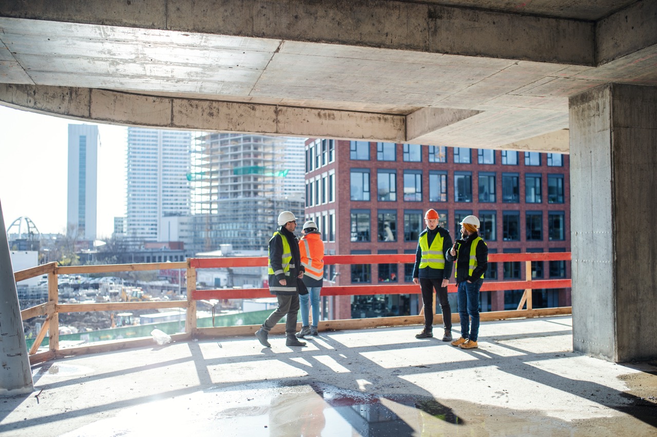A group of engineers standing on a construction site, talking. Construction site ID badges. ID badge creation system for construction sites. Secure photo ID badges for construction workers. Proximity-enabled construction site ID badge.