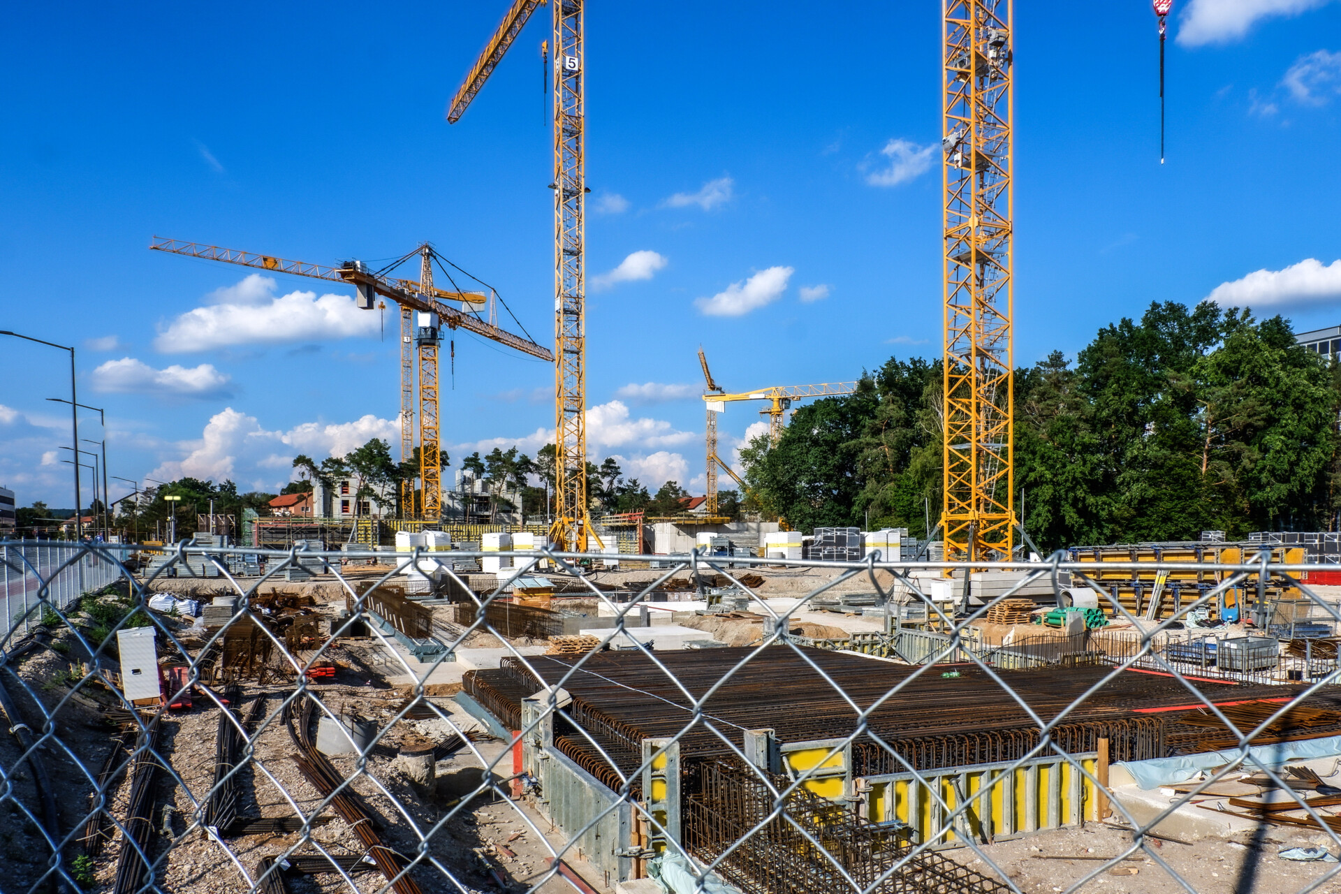 Fenced construction site with multiple cranes, building materials, and jobsite access barriers