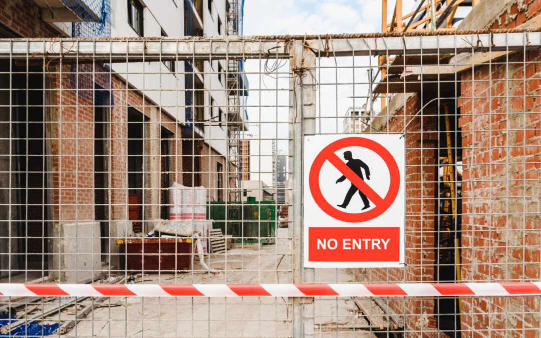 No entry sign on fenced construction site with visible building materials and blocked access